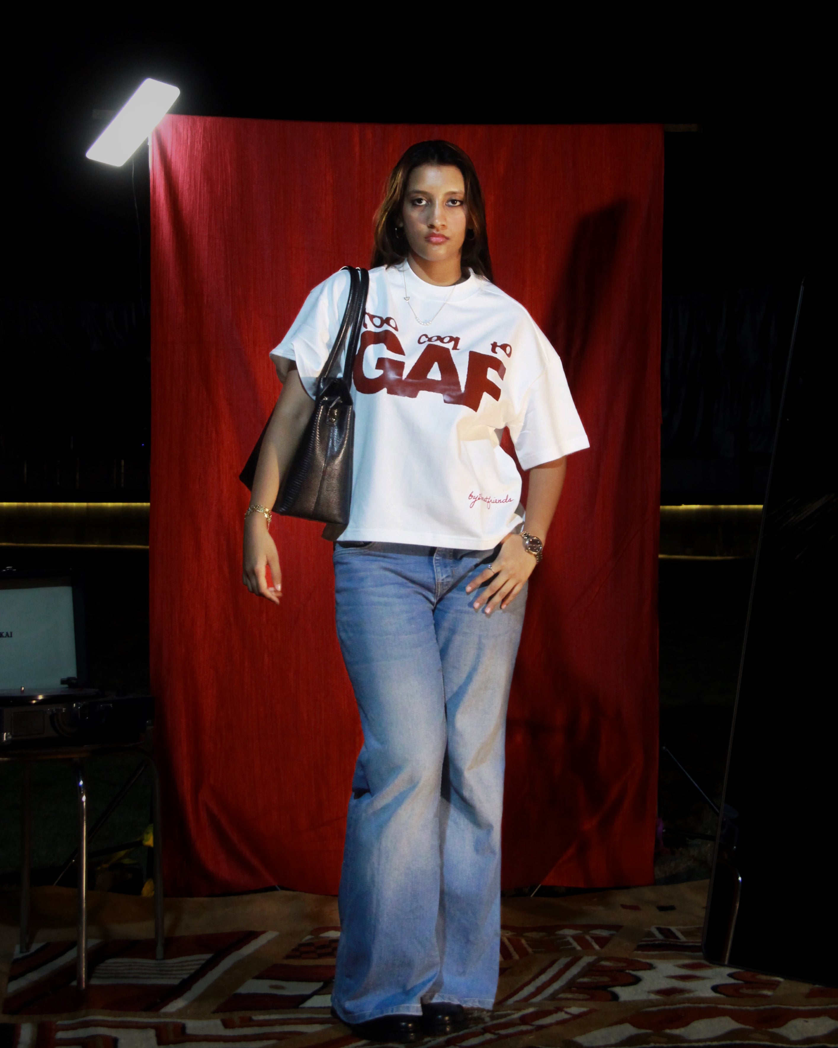Woman wearing a white t-shirt with text and blue jeans standing in front of a red curtain.